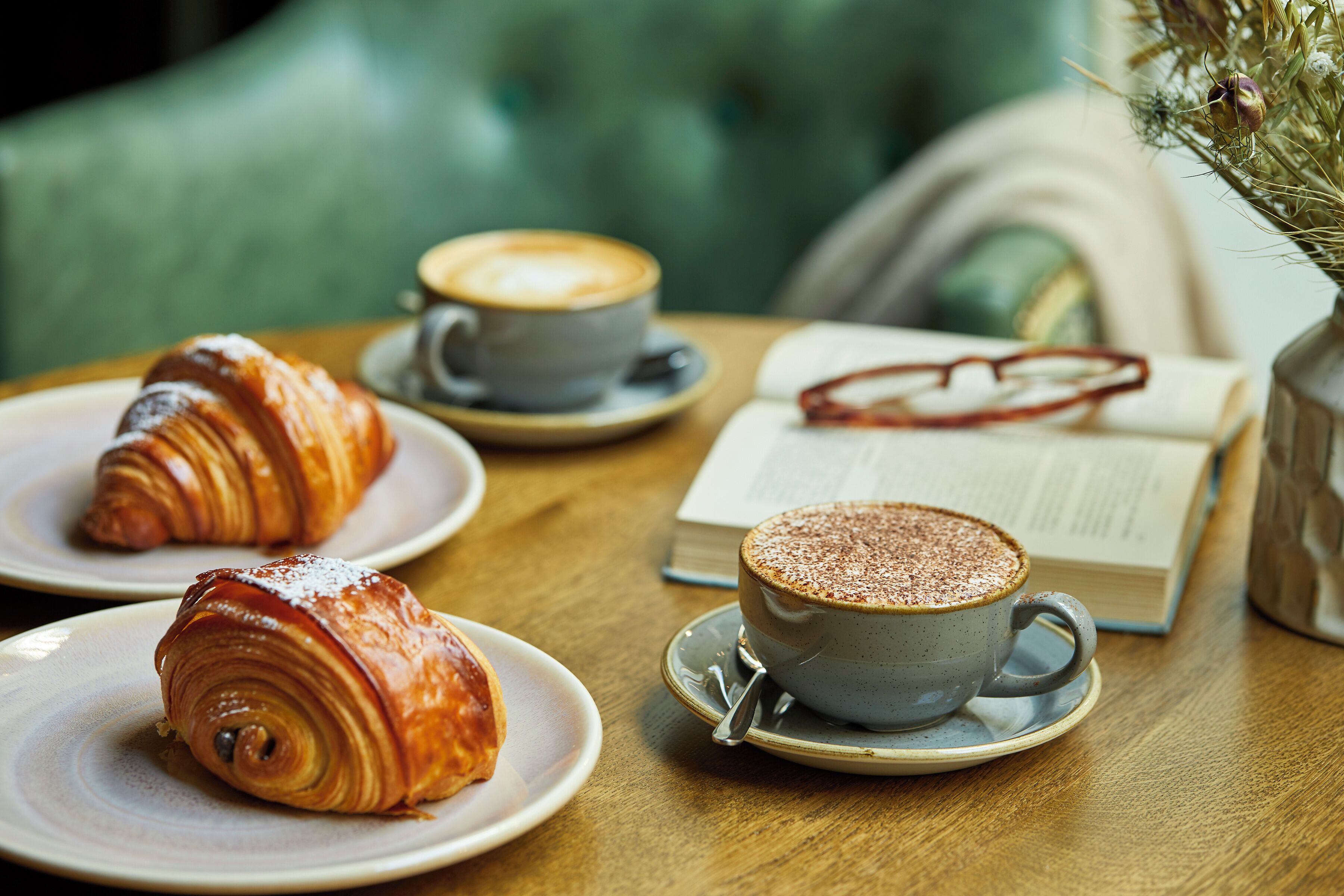 Una mesa con croissants, una taza de café y un libro.