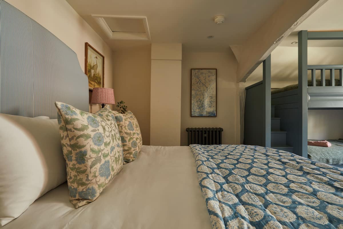 Un dormitorio con cama, almohadas, un radiador, un cuadro enmarcado y una escalera.
