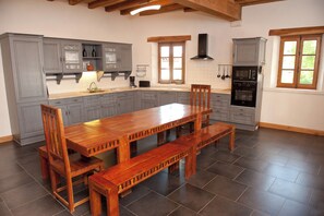 A spacious kitchen with grey cabinets, a wooden dining table, and a built-in oven. - Gîte la Maison du Randonneur (Castelnau-sur-l'Auvignon)