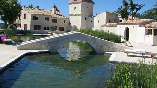 Un puente de piedra sobre aguas tranquilas, con una torre y edificios al fondo.