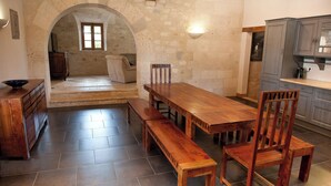 Un comedor amplio con una larga mesa de madera y bancos, paredes de piedra y vistas a otra habitación a través de un arco.