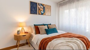 Une chambre à coucher avec un lit, une table de chevet avec une lampe et une œuvre d’art abstraite accrochée au mur.