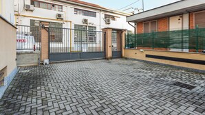 Une cour avec un sol pavé, une entrée fermée par un portail et un bâtiment doté de nombreuses fenêtres et de plusieurs unités de climatisation.