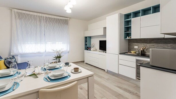 Une cuisine moderne avec des meubles blancs, un four encastré et un coin repas avec une table mise pour deux personnes.