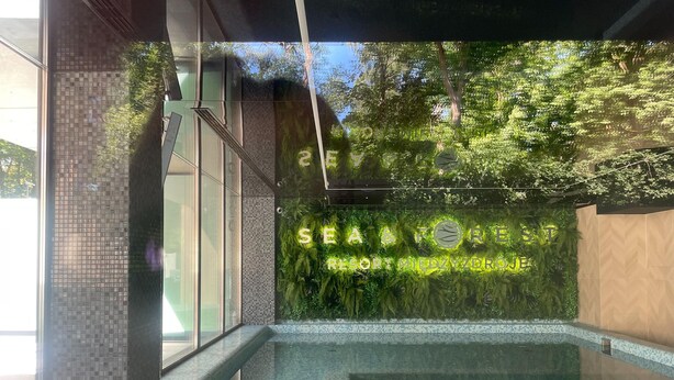 A modern indoor pool area with a glass wall reflecting trees and a sign reading "SEA & FOREST RESORT MIEDZY ZDROJE". - Luxurious Apartment in Miedzyzdroje, SPA Zone (Międzyzdroje)