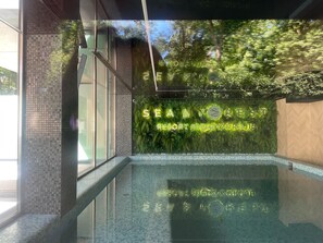 Ein moderner, überdachter Poolbereich mit Glaswand, die Bäume reflektiert, und einem Schild mit der Aufschrift "SEA & FOREST RESORT MIEDZY ZDROJE".