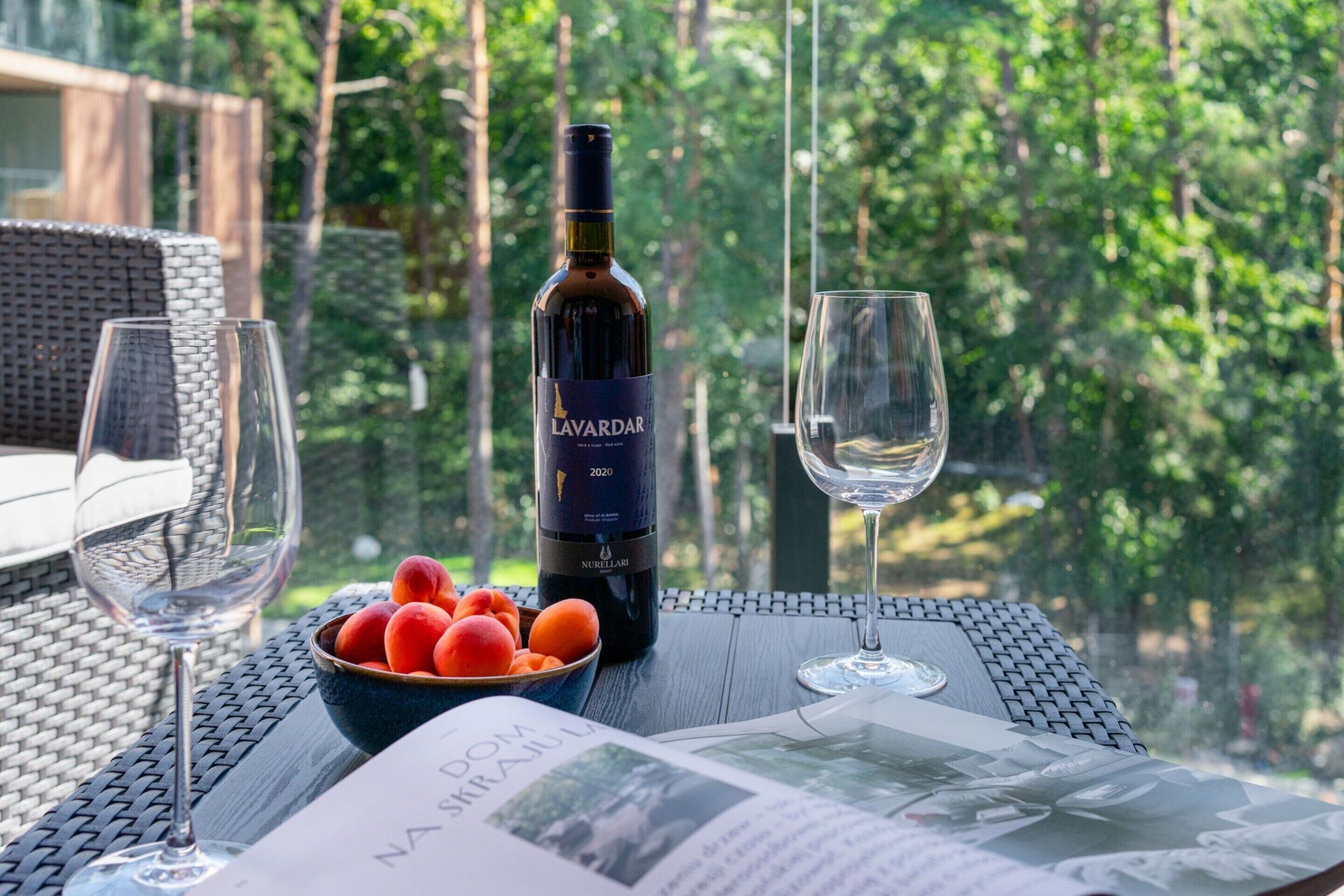 A bottle of Lavardar 2020 wine, a bowl of fruit, and two wine glasses on a table with a magazine.