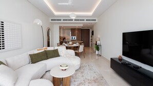 Un salon moderne avec un canapé d’angle, un téléviseur à écran plat et un coin repas à l’arrière-plan.
