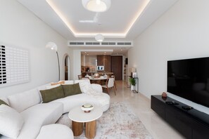 Ein modernes Wohnzimmer mit einer Eckcouch, einem Flachbildfernseher und einem Essbereich im Hintergrund.