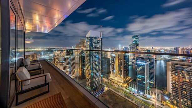 Un immeuble de grande hauteur offrant une vue panoramique sur la ville, avec un balcon doté de mobilier moderne.