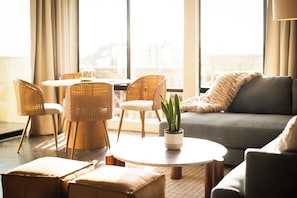 A modern living room with wicker furniture, a grey sofa, and a potted plant on a round table. - Pier View Sunset - Ocean Front, Patios, Location, Views (San Diego)