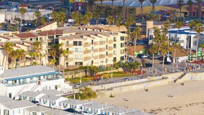Een hotel met meerdere verdiepingen en balkons, gelegen nabij een strand met palmbomen en een promenade.