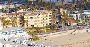 A multi-story hotel with balconies, located near a beach with palm trees and a boardwalk. - Pier View Sunset - Ocean Front, Patios, Location, Views (San Diego)