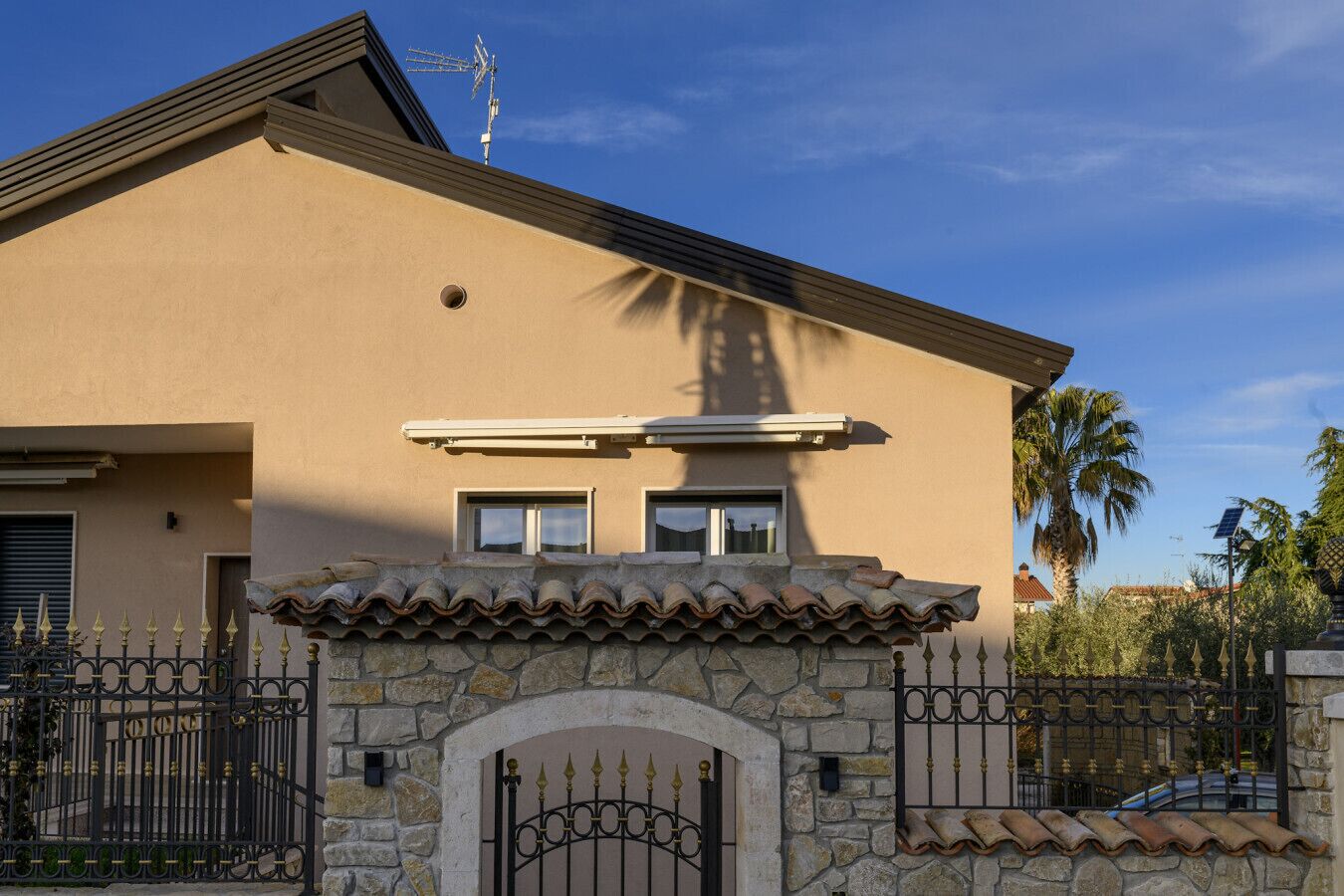Una casa a due piani con facciata in pietra, tetto in tegole e cancello in metallo.