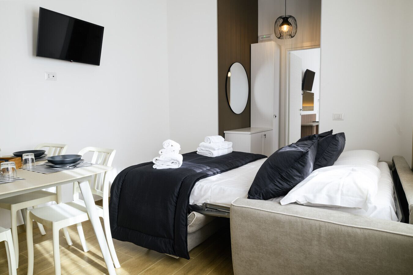 A hotel room with a bed, a desk with chairs, a television, and a mirror.