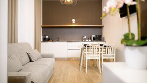 Een moderne woonkamer met een bank, een eettafel met stoelen, een keukenhoek met een magnetron en koffiezetapparaat, en een hanglamp.