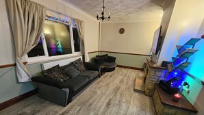Ein Wohnzimmer mit grauem Sofa, gemusterten Kissen, einem Kamin aus Stein und einem blauen Regal.