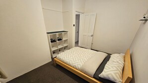Ein kleines, aufgeräumtes Schlafzimmer mit einem Einzelbett, einem Einbauschrank und einem Nachttisch mit Lampe.