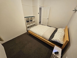Een kleine, verzorgde slaapkamer met een enkel bed, een inbouwkast en een nachtkastje met een lamp.
