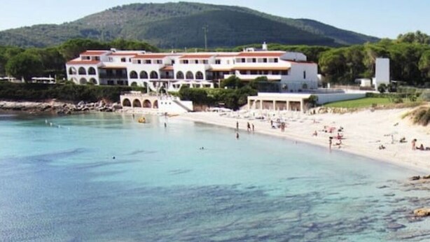 Un hôtel situé sur la côte, doté d’un grand bâtiment, d’une plage et d’une eau cristalline.