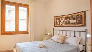 Une chambre à coucher avec un lit, une table de chevet, une tapisserie murale et une fenêtre avec des rideaux.
