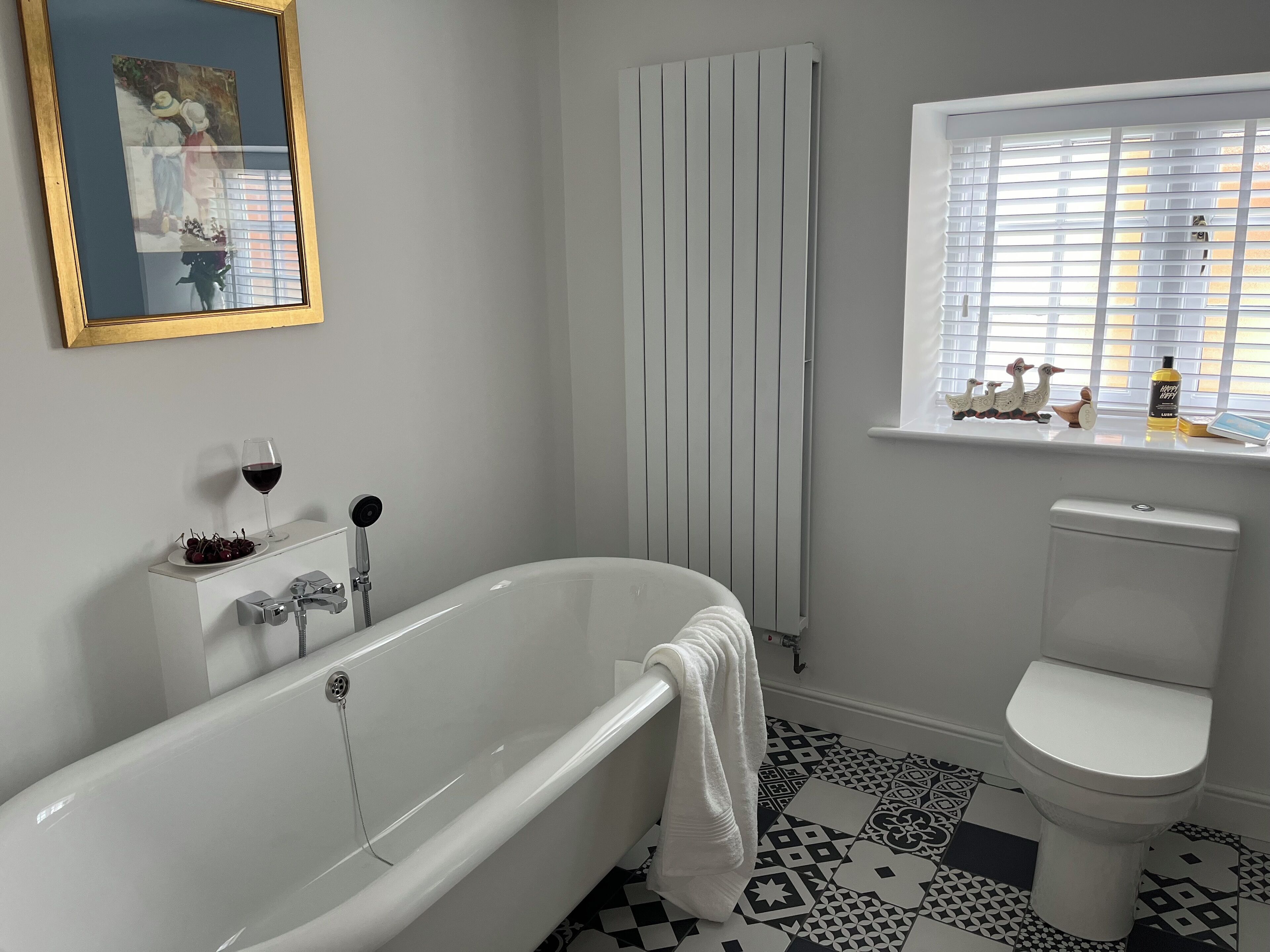 Une salle de bain avec une baignoire blanche, des toilettes et une fenêtre avec des stores.