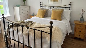 Een slaapkamer met een bed, nachtkastje, kaptafel, raam en een ingelijst schilderij aan de muur.