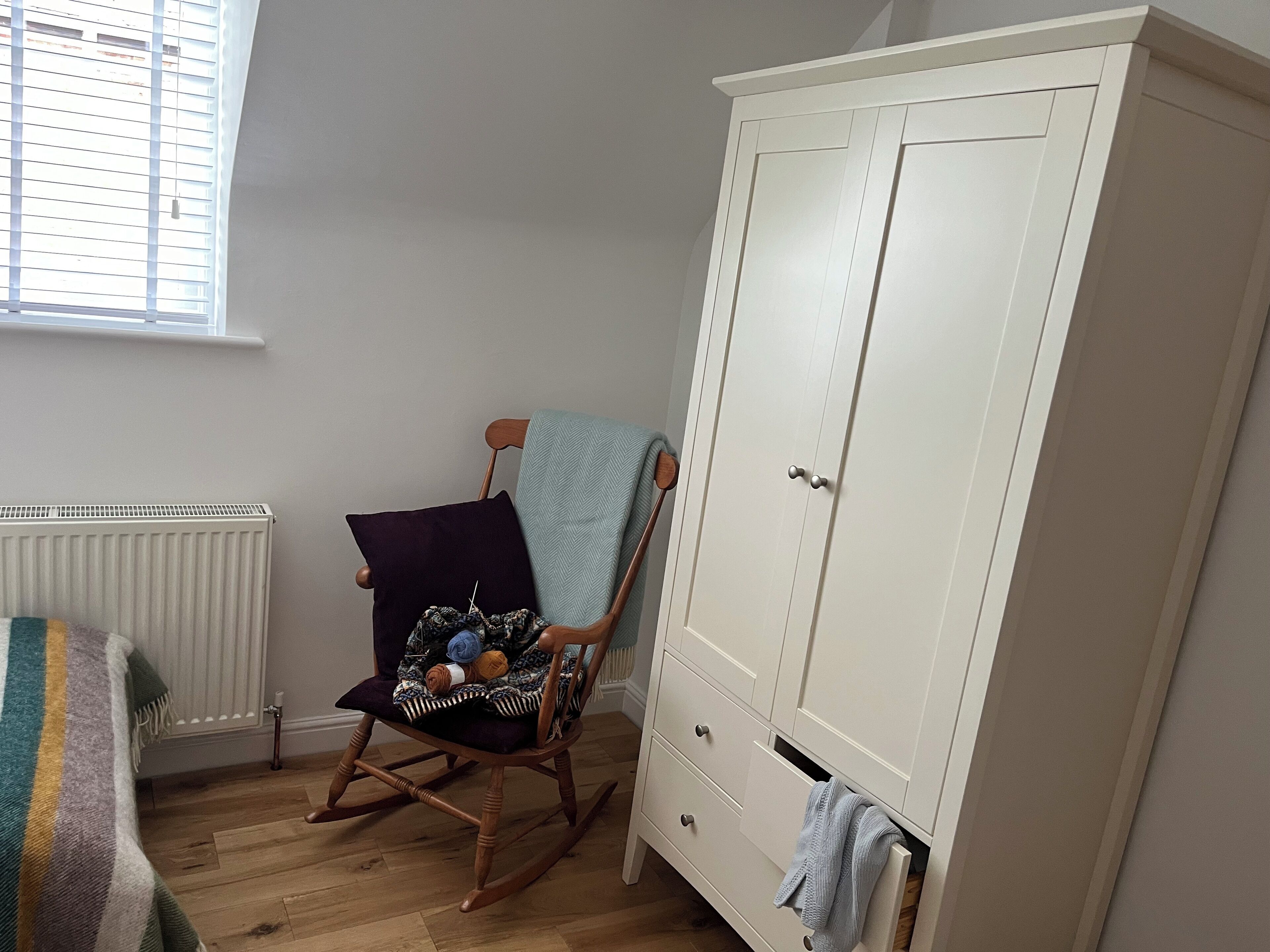 A room with a rocking chair, a white wardrobe, and a radiator.
