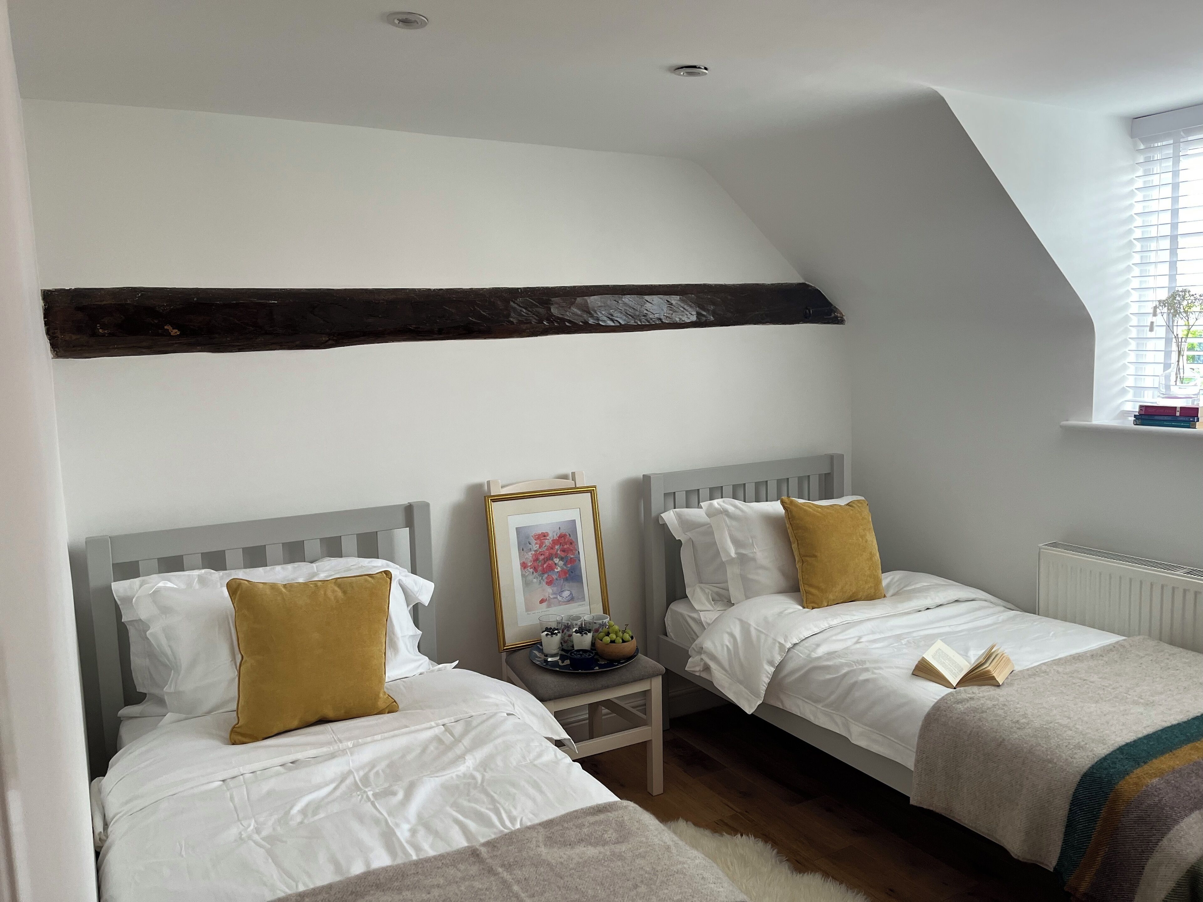 Quarto com duas camas, um quadro na parede e uma janela com persianas.
