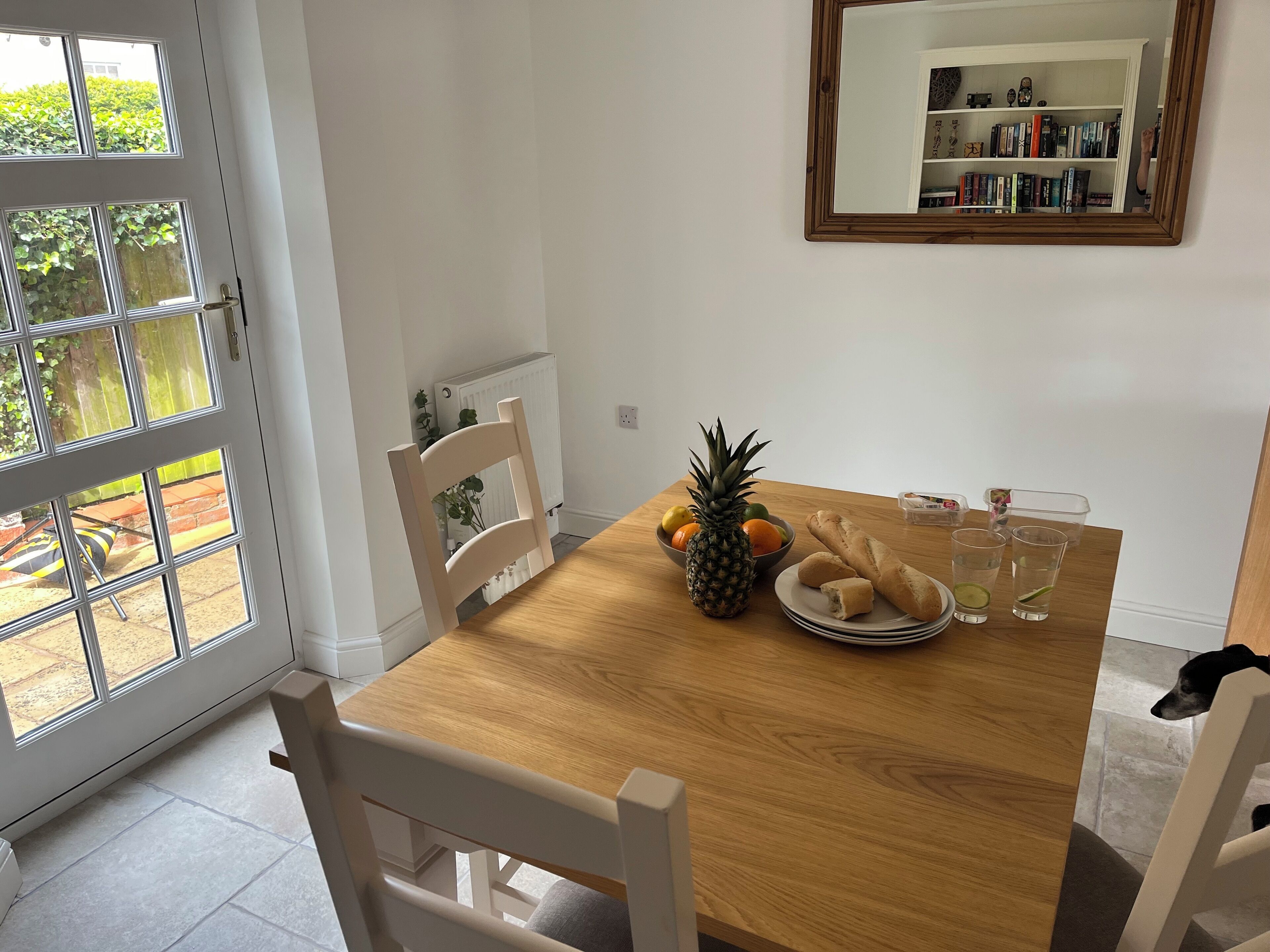 Un coin repas avec une table en bois, des chaises, un panier de fruits, une miche de pain et un verre d’eau.