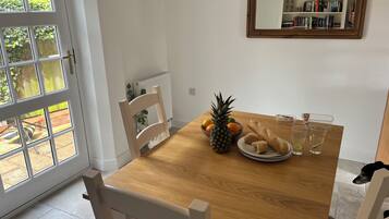 Un coin repas avec une table en bois, des chaises, un panier de fruits, une miche de pain et un verre d’eau.