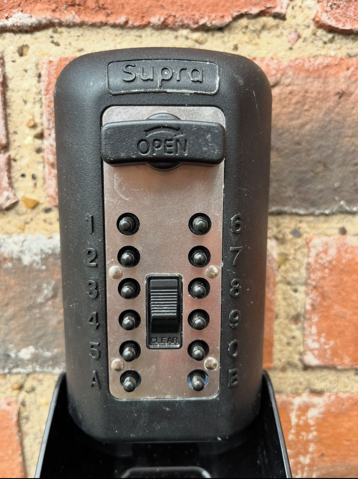 A black intercom with the brand 'Supra' and an 'OPEN' sign, featuring a keypad with numbers and letters.