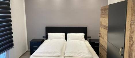 Un dormitorio moderno con cama doble, mesita de noche, armario y ventana con persianas.