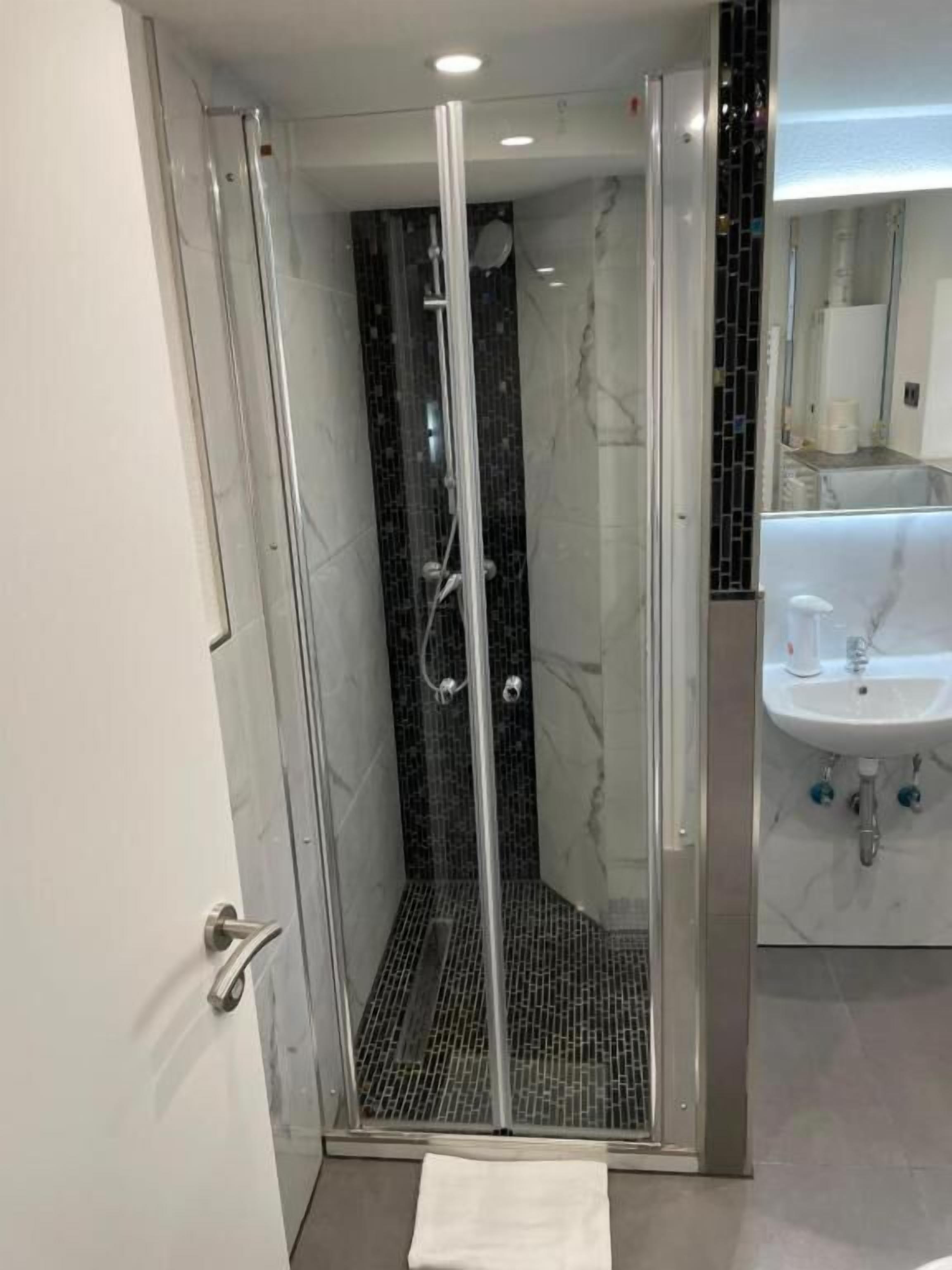 Un baño moderno con cabina de ducha de vidrio, lavamanos blanco y salpicadero de mármol.