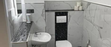 Een moderne badkamer met een wit wastafelmeubel, een toilet en een douche.