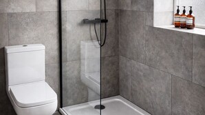 Een moderne badkamer met een douchecabine van glas, een wit toilet en een raam met uitzicht.