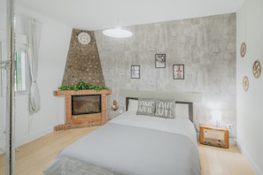 Un dormitorio con cama, chimenea de ladrillo, un reloj de pared y cuadros enmarcados.
