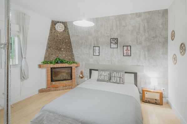 A bedroom with a bed, a brick fireplace, a wall clock, and framed pictures.