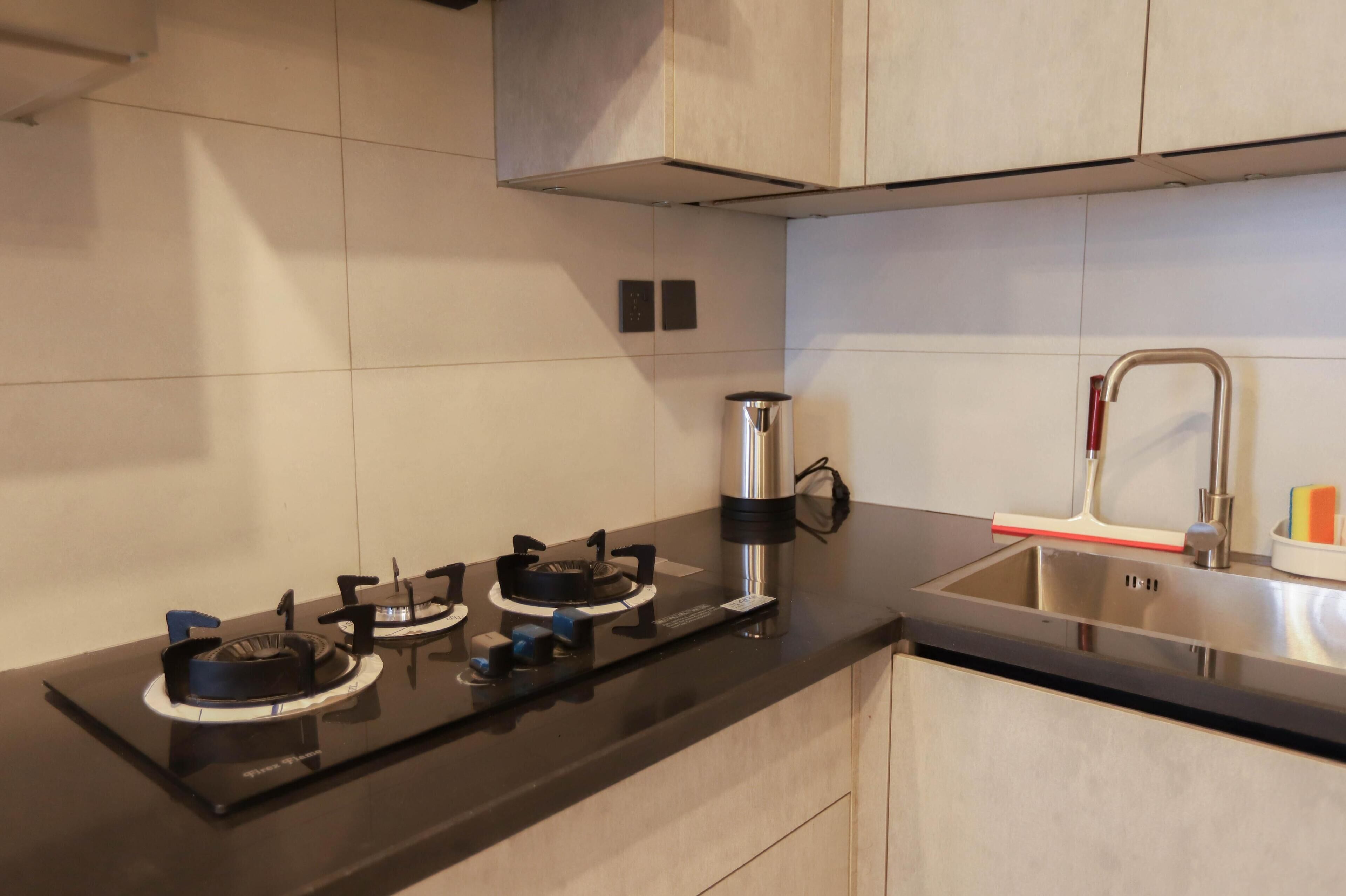Una cucina moderna con un piano di lavoro nero, piano cottura in acciaio inossidabile e lavello con rubinetto rosso.
