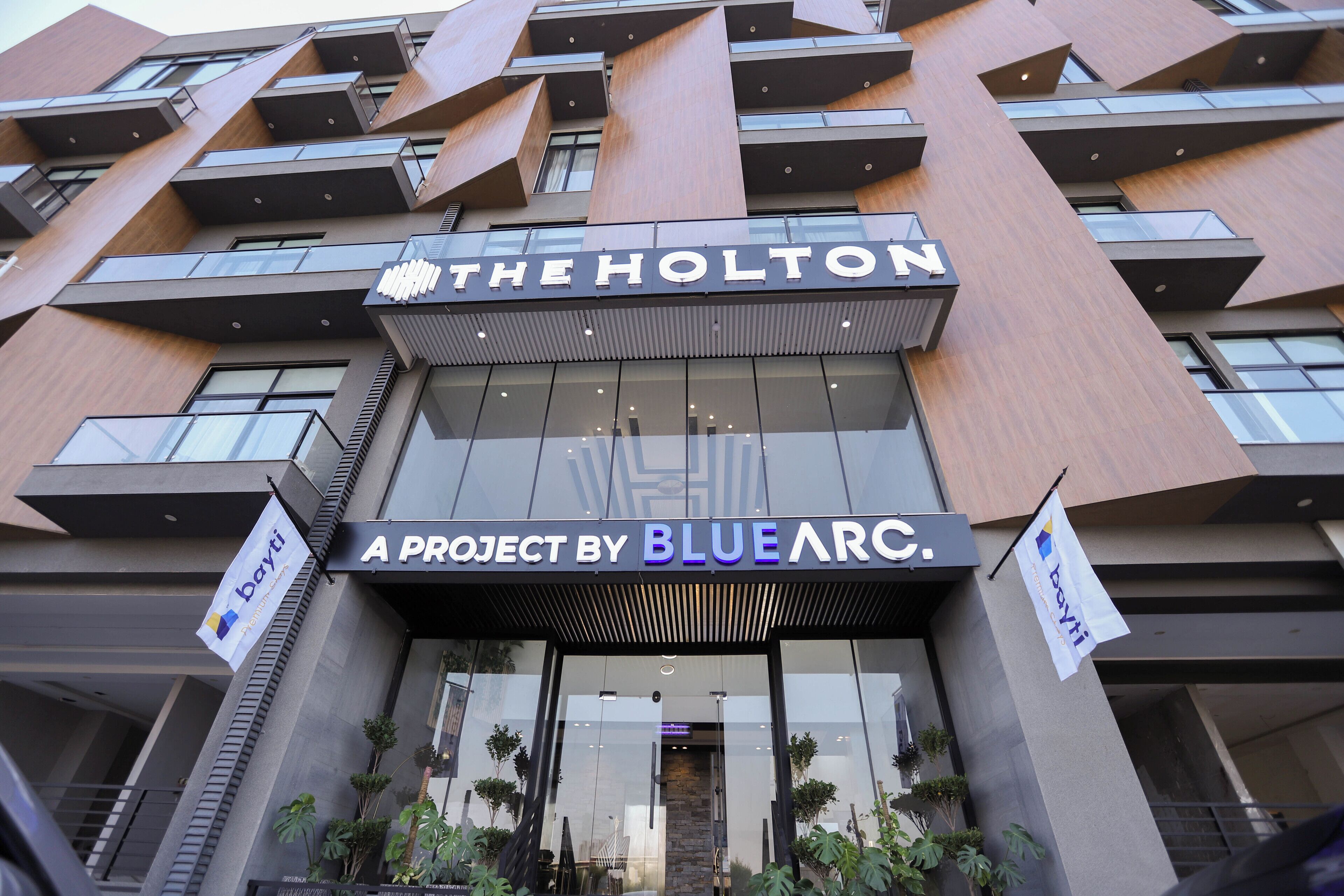 Ein moderner Hotel Eingang mit einem Schild, auf dem 'The Holton' und 'A Project by BlueArc' steht.