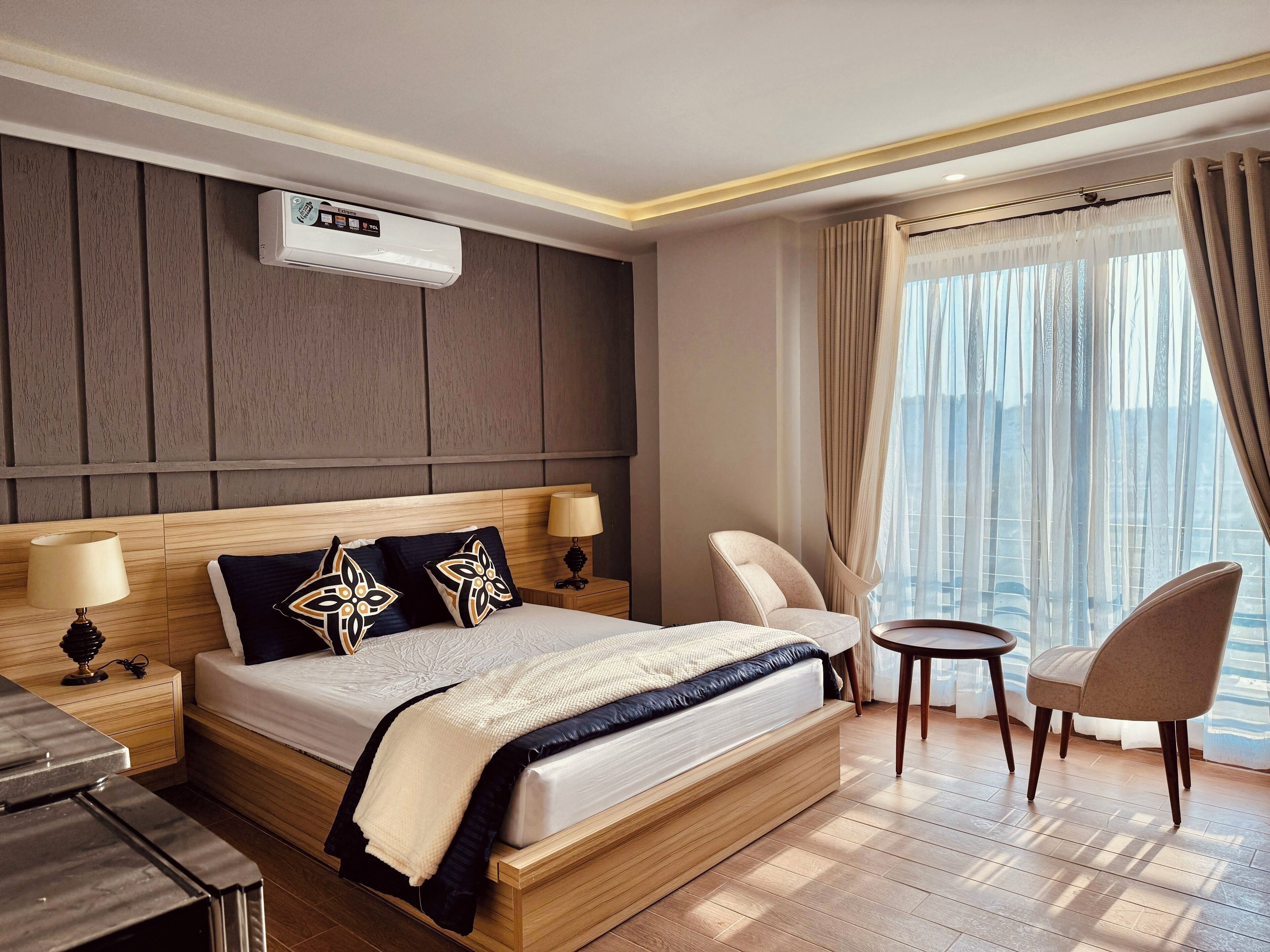 Une chambre d’hôtel avec un lit en bois, deux tables de chevet avec des lampes, une petite table ronde et une chaise.