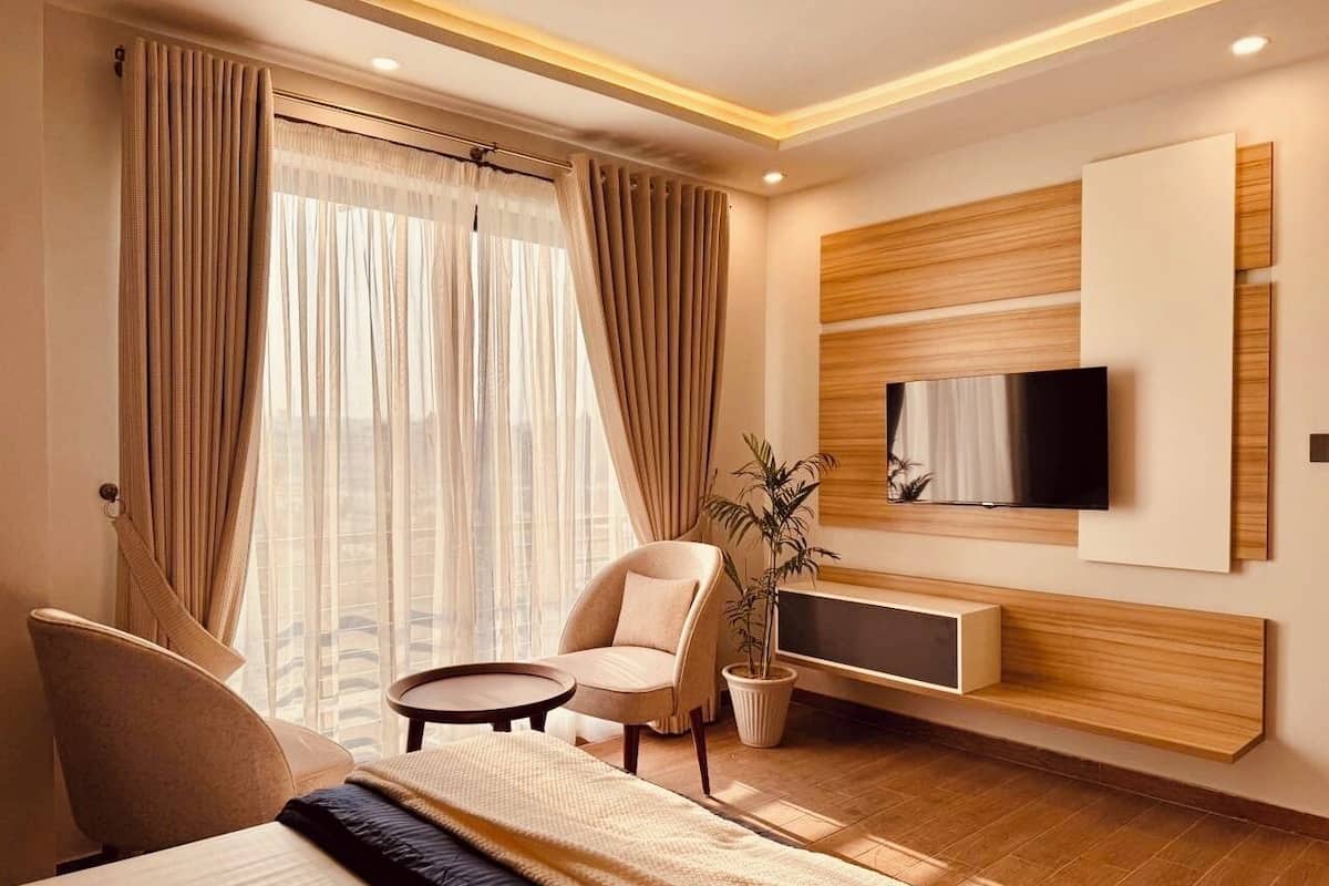 Ein modernes Hotelzimmer mit einem großen Bett, einem runden Tisch, einem Sessel, einem Fernseher und einer Zimmerpflanze.