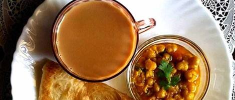 A plate with a cup of tea, a bowl of chickpeas, and a piece of flatbread.