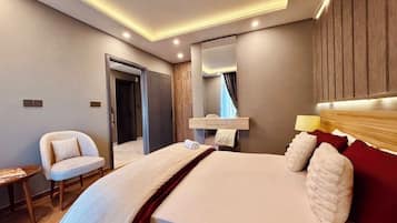 A modern hotel room with a large bed, a bedside table, a chair, a mirror, and a wooden headboard.