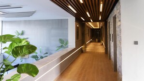Un couloir moderne avec des lambris en bois au plafond, un long comptoir d’accueil et des plantes en pot.