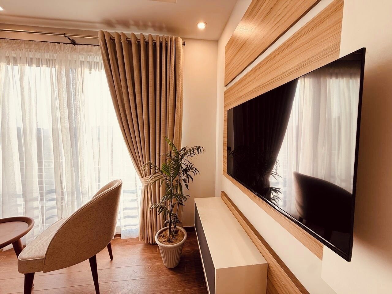 A modern living room with a large flat-screen TV, a wooden TV stand, a potted plant, a sofa, and a dining table.