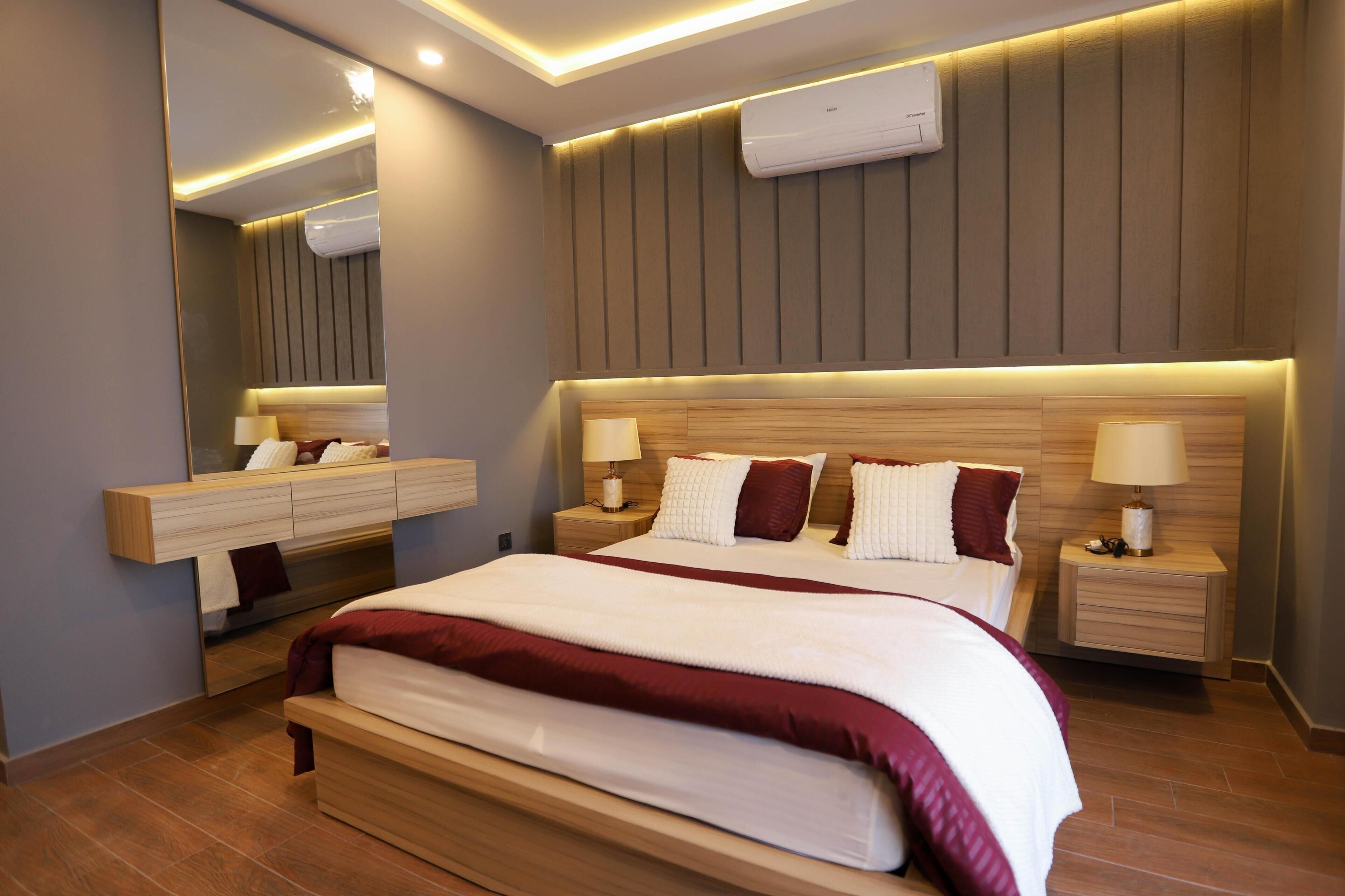 A modern hotel room with a large bed, bedside tables with lamps, a built-in wardrobe, and a large mirror.