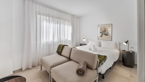 A modern hotel room with a sofa, a bed, a painting, and two bedside lamps.