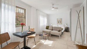 A modern living room with a sofa, a dining table with chairs, a standing lamp, and a floor lamp.