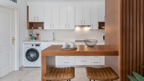 A modern kitchen with white cabinets, a wooden island, two stools, and a washing machine.